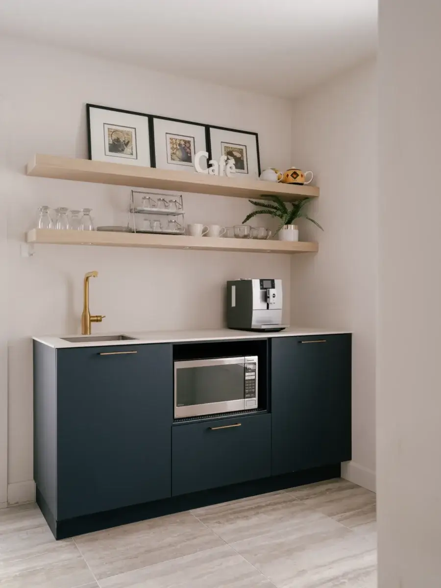 Coin café avec armoires bleu nuit, comptoir blanc, robinet doré et étagères en bois clair – cuisine Kamouraska par Mathurin cuisines & salles de bains.