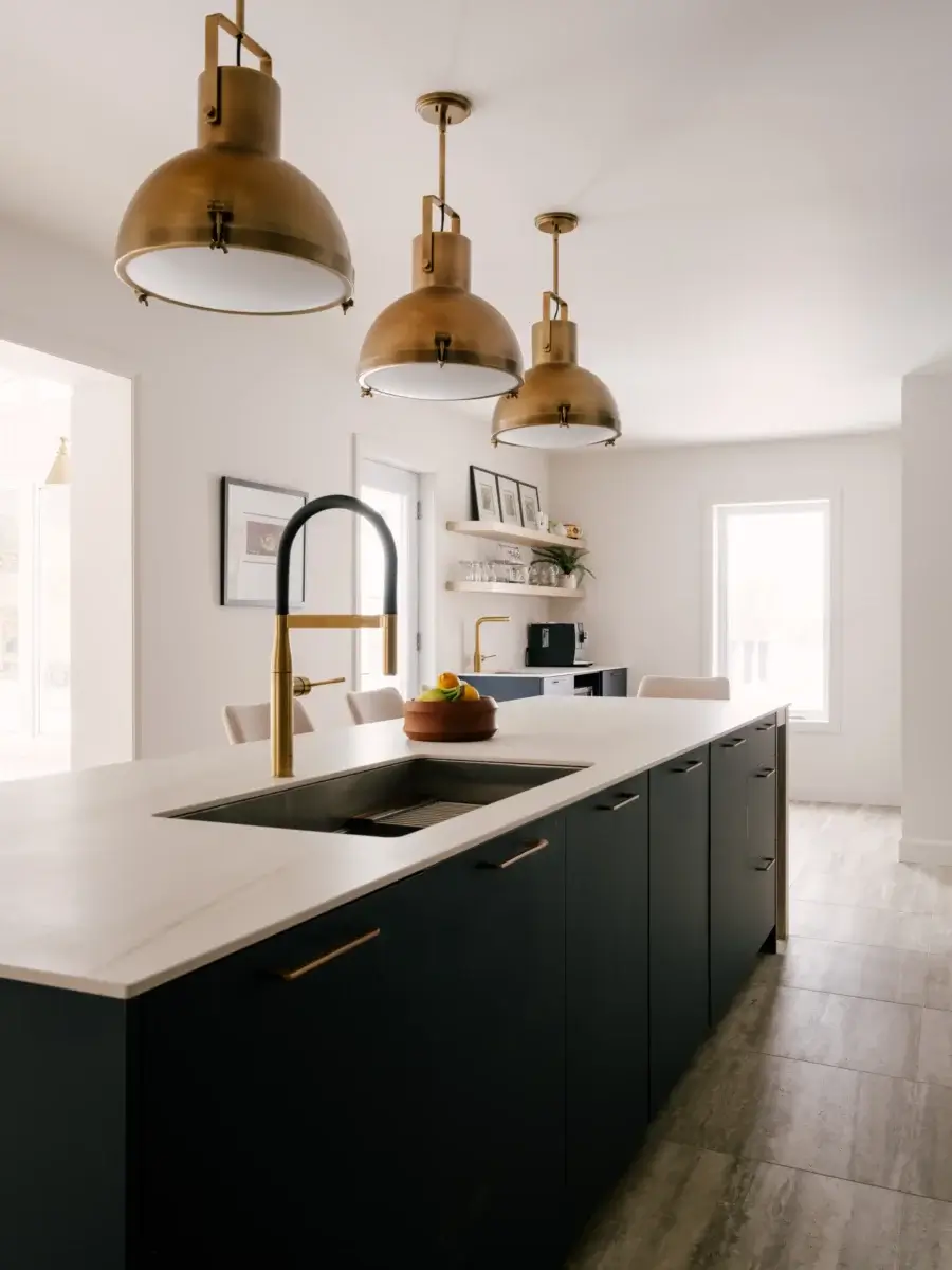 Îlot de cuisine avec armoires bleu foncé, comptoir blanc effet marbre, robinet doré et suspensions en laiton – cuisine Kamouraska.