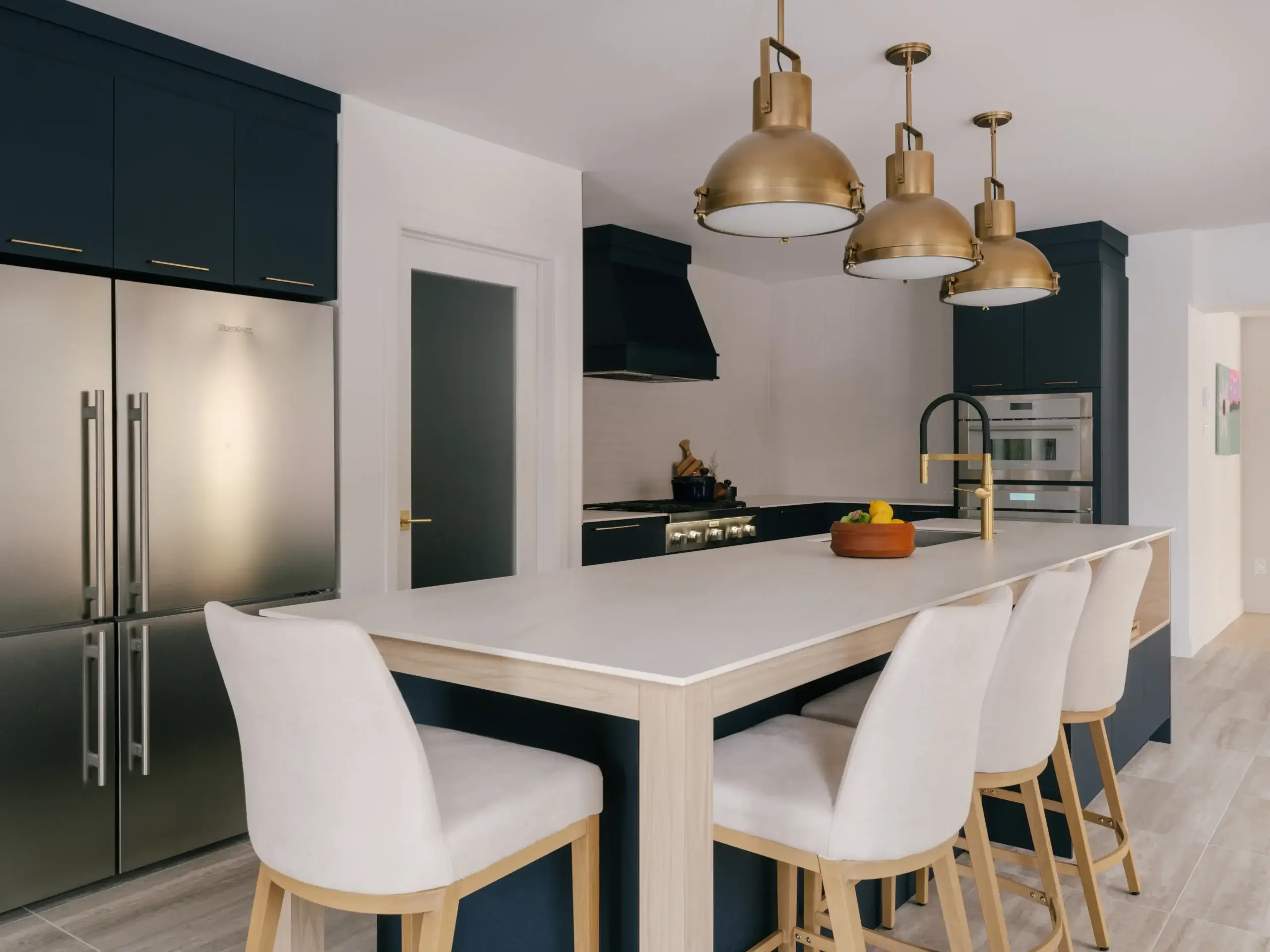 Cuisine ouverte avec îlot central blanc, chaises rembourrées et armoires bleu foncé – projet Kamouraska.
