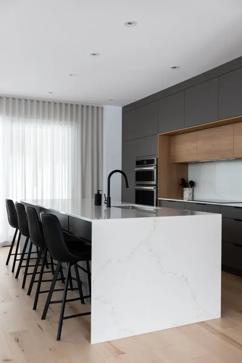 Îlot de cuisine contemporain avec retombée en quartz blanc veiné, robinet noir et tabourets en cuir noir – cuisine Du Geai-bleu.