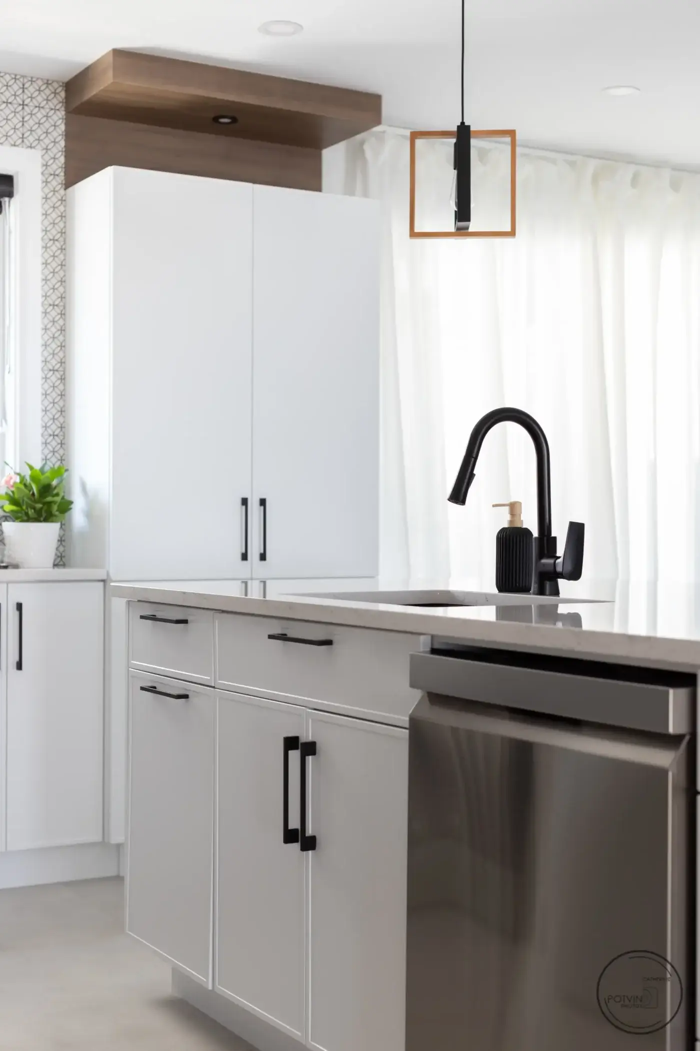 Armoires blanches sur mesure avec poignées noires, comptoir en quartz et robinetterie noire mate – cuisine conçue par Armoires Mathurin.