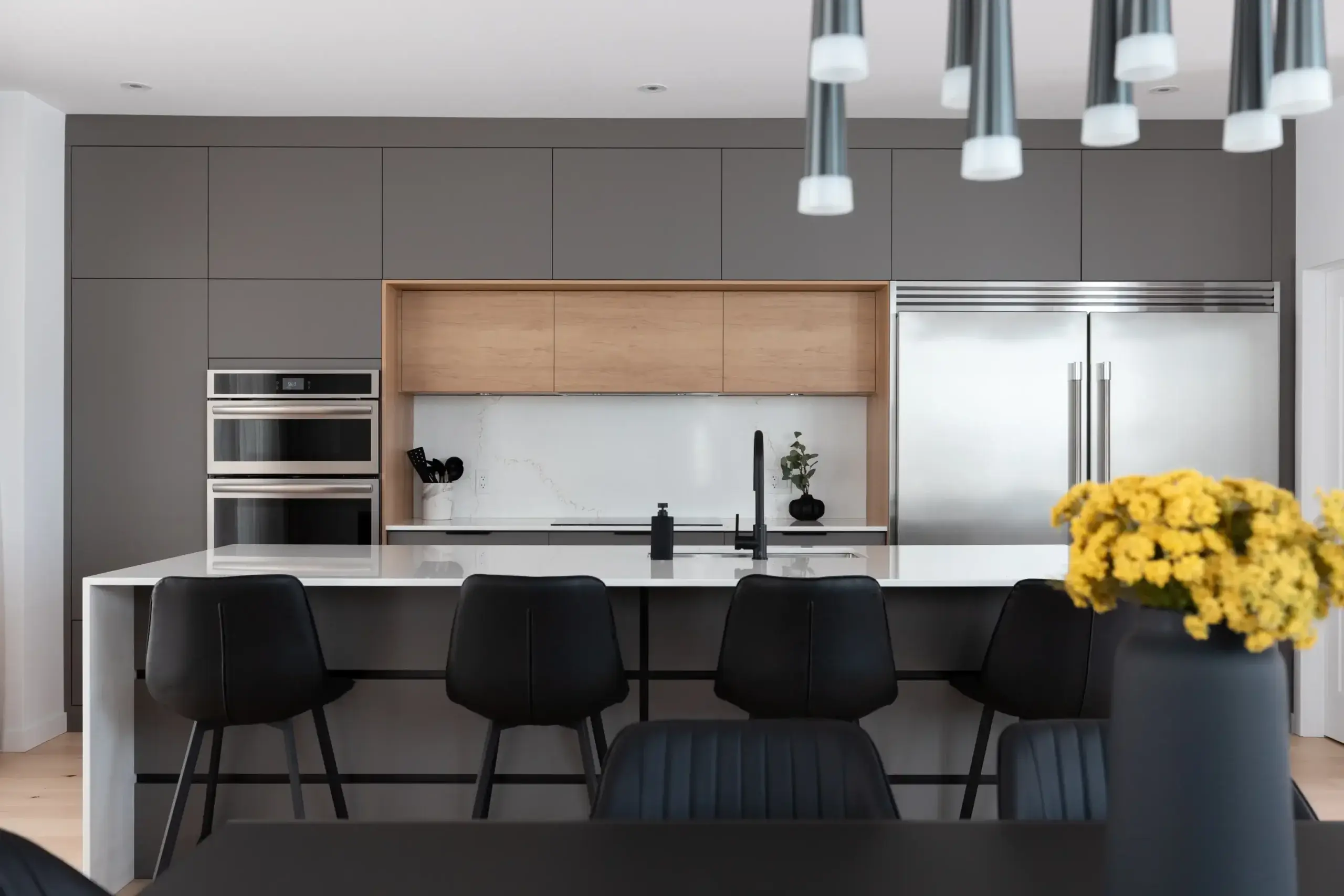 Cuisine haut de gamme avec armoires gris charbon, modules en bois naturel, électroménagers intégrés et îlot central en quartz – projet Du Geai-bleu par Armoires Mathurin.