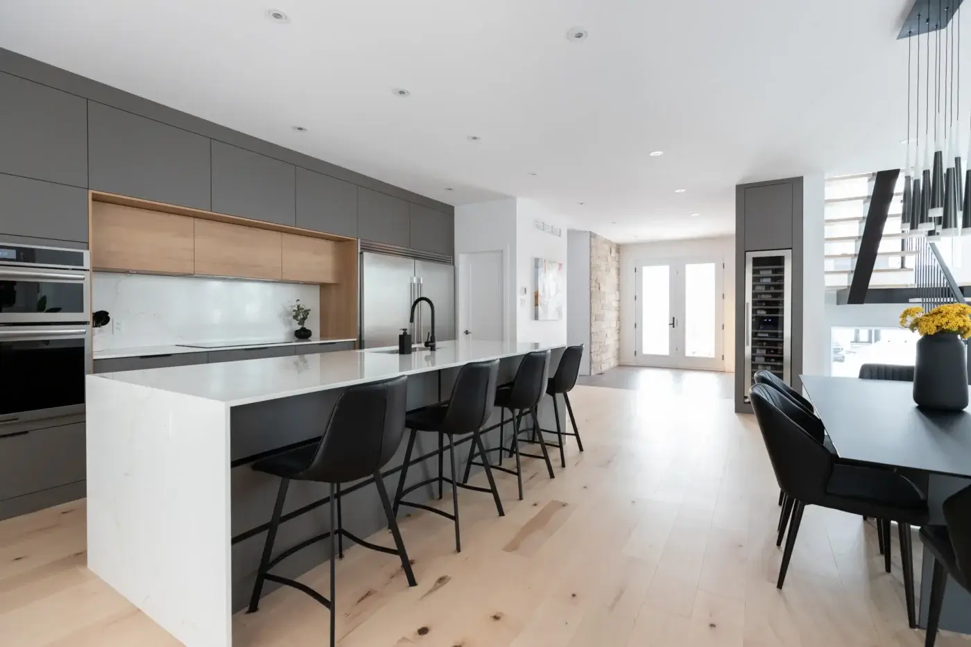 Cuisine en aire ouverte avec grand îlot, armoires pleines hauteur, salle à manger attenante et escalier flottant – design signé Mathurin cuisine & salles de bains.