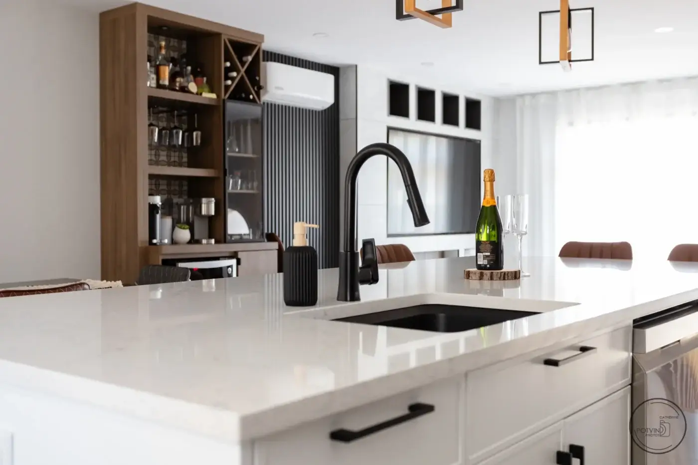 Îlot de cuisine en quartz avec évier noir, robinet contemporain et vue sur cellier et coin café intégrés – réalisation Armoires Mathurin à Lévis.