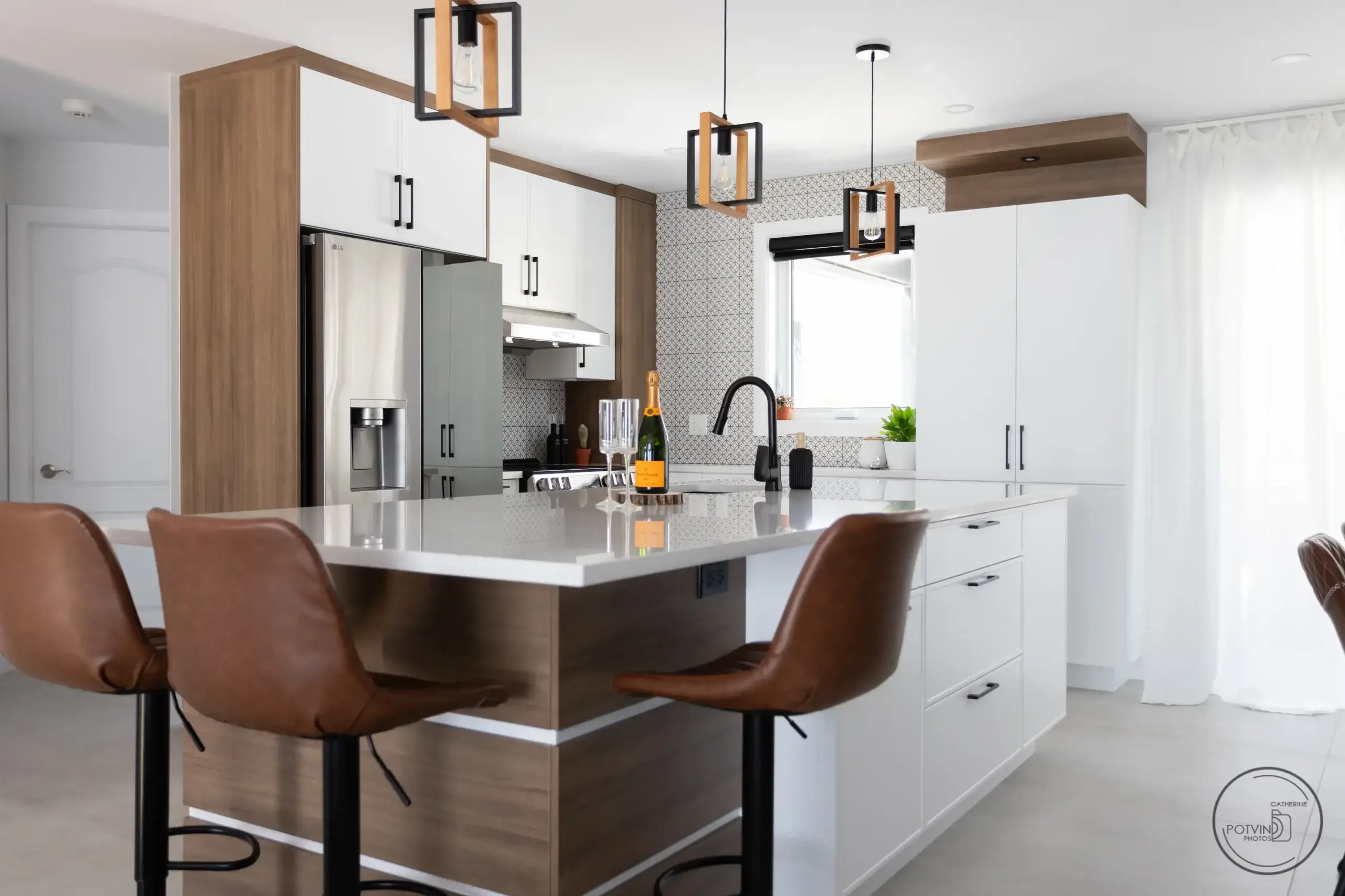 Cuisine moderne avec îlot central, armoires blanches et en bois, comptoir en quartz et chaises en cuir brun, conçue par Armoires Mathurin.