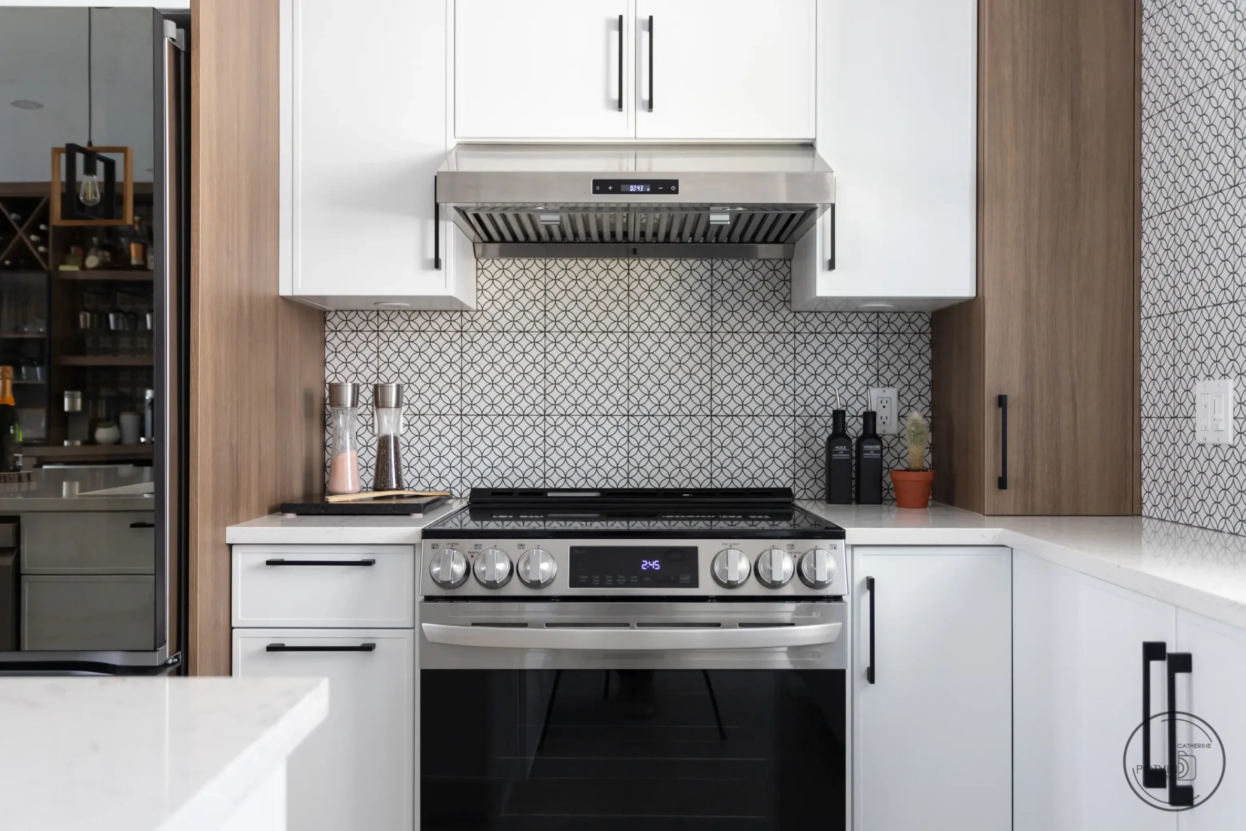 Cuisinière en acier inoxydable avec hotte encastrée, dosseret à motifs géométriques et armoires blanches et bois – projet Armoires Mathurin.