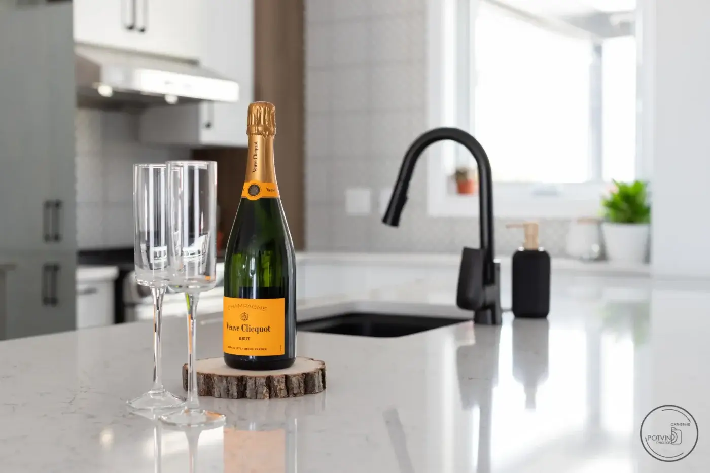 Plan rapproché sur comptoir de cuisine en quartz avec évier noir, robinet contemporain et flûtes de champagne – design Armoires Mathurin.