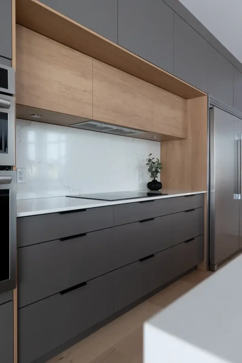 Zone cuisson avec hotte dissimulée, dosseret en quartz blanc et armoires sans poignées – réalisation sur mesure Armoires Mathurin.