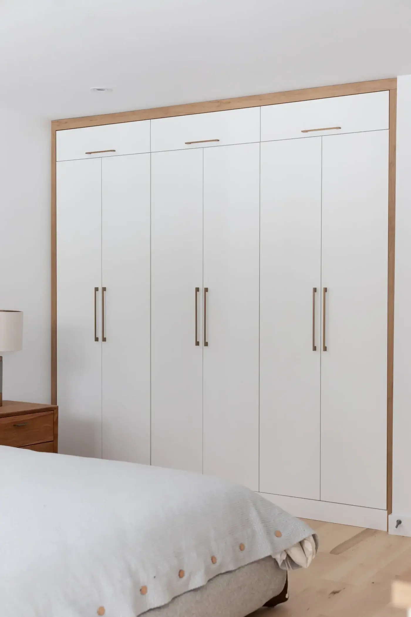 Garde-robe sur mesure blanche à Québec avec encadrement bois naturel et poignées dorées verticales.