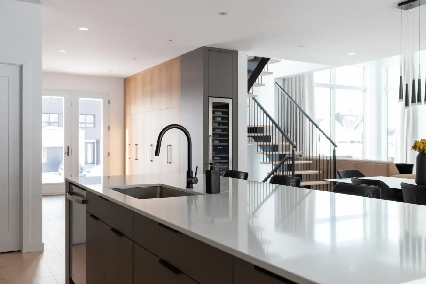 Vue de la cuisine vers le mobilier d’entrée sur mesure, incluant des armoires pleine hauteur en bois clair.