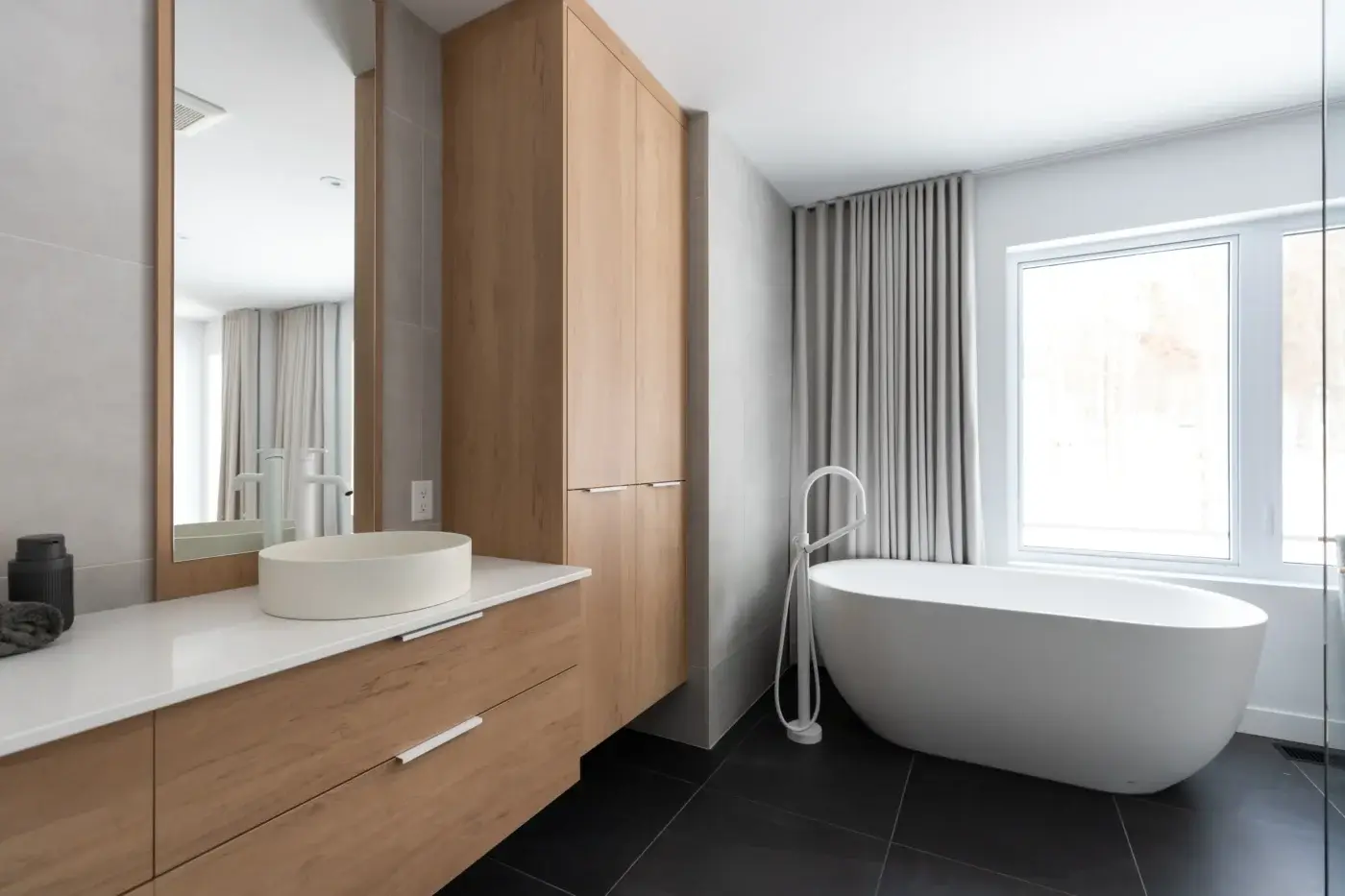 Salle de bain de maison neuve à Québec avec bain autoportant et mobilier sur mesure effet bois.