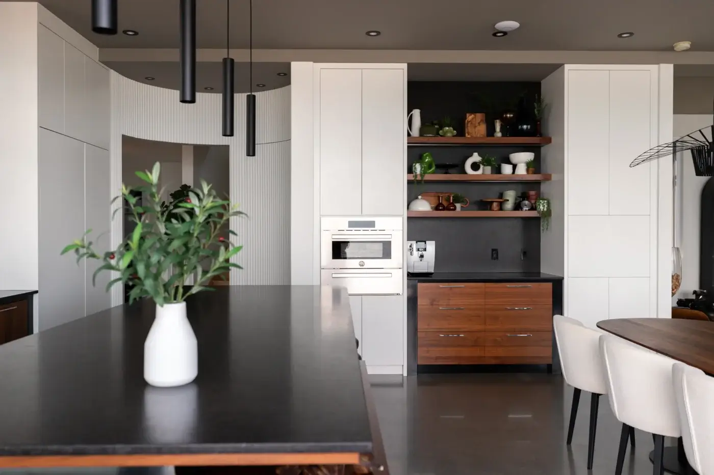 Cuisine moderne avec armoires blanches, four encastré et étagères ouvertes en bois.