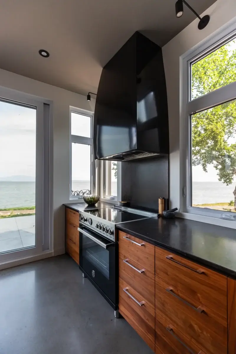 Cuisinière avec hotte décorative noire et vue sur le fleuve à travers les fenêtres.