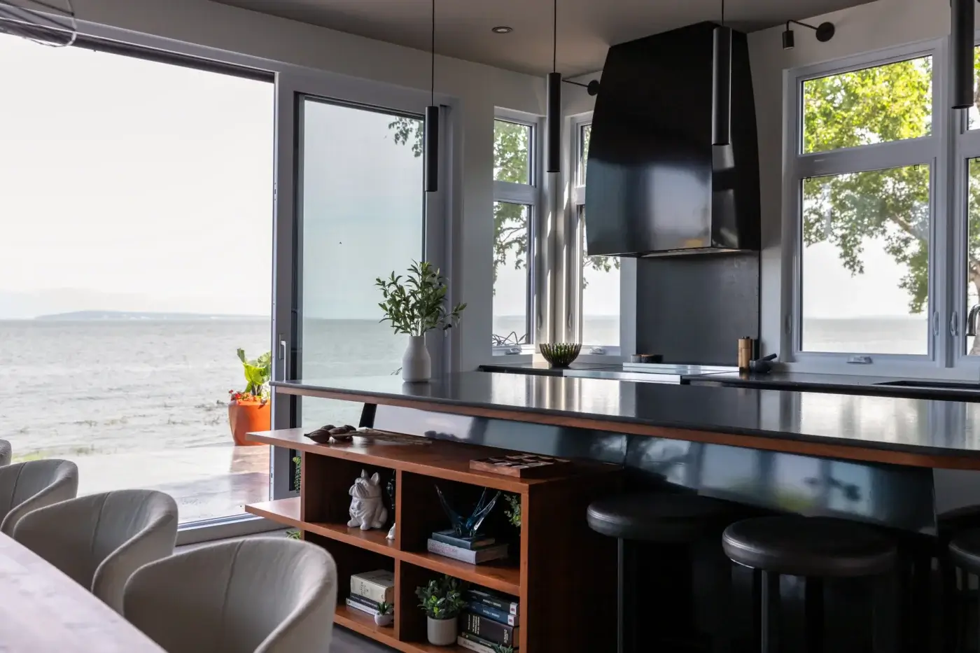 Îlot de cuisine en bois et noir avec étagères ouvertes face à une grande baie vitrée.