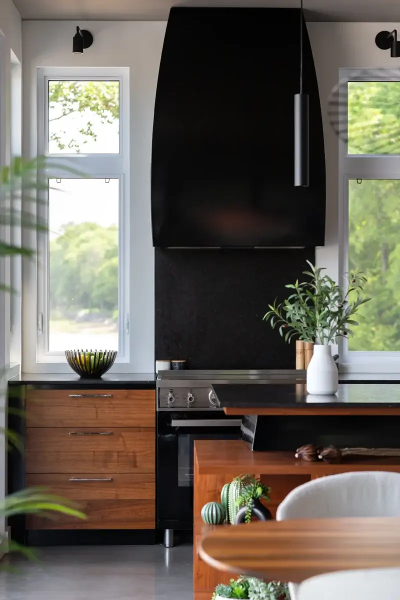 Hotte noire moderne au-dessus d’une cuisinière encastrée avec armoires en placage de bois.
