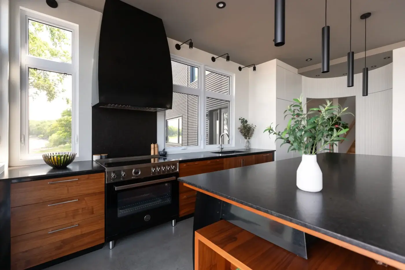 Cuisine complète avec îlot noir et bois, hotte décorative et coin repas.