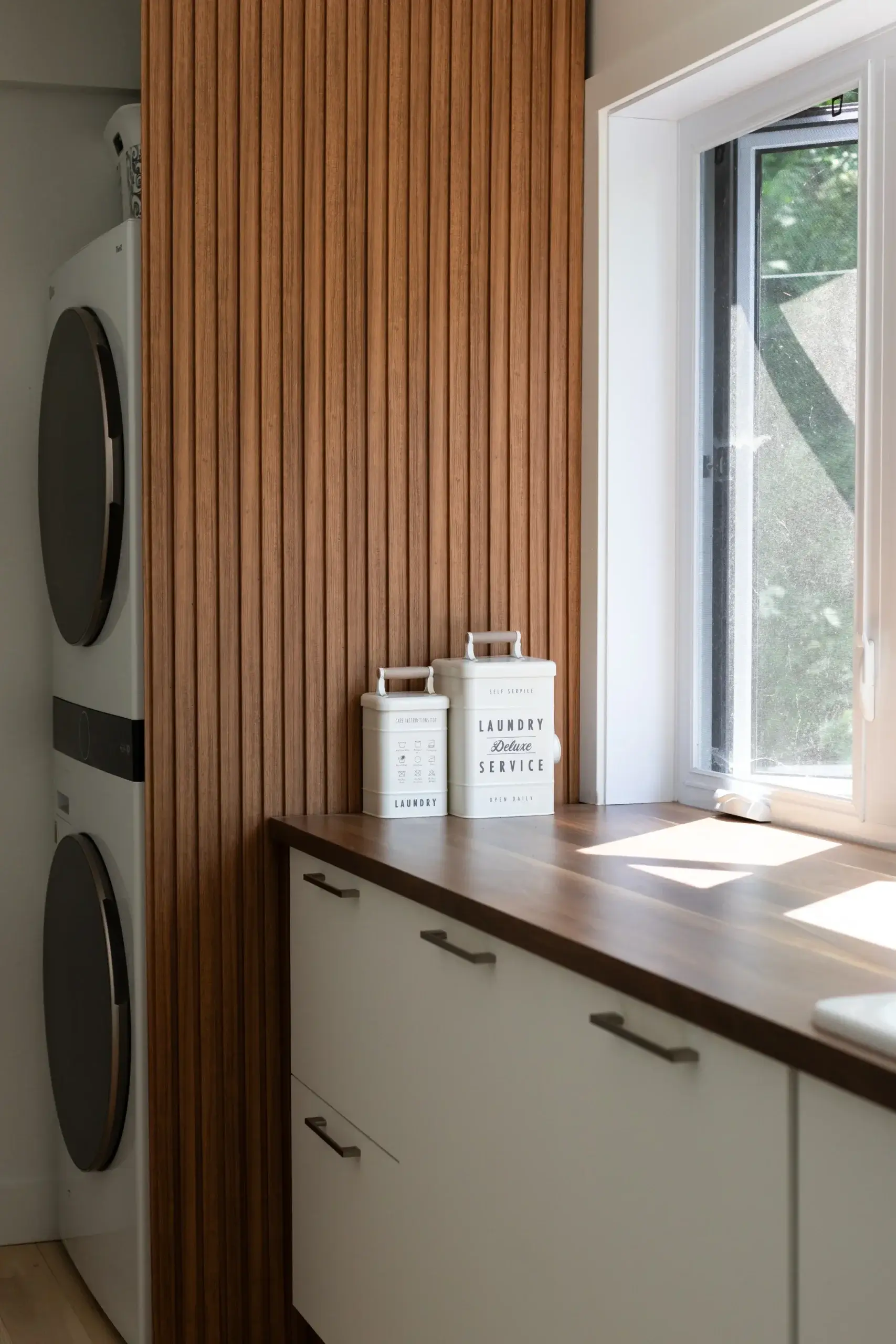 Salle de lavage avec laveuse sécheuse superposées et panneau en lattes de bois.