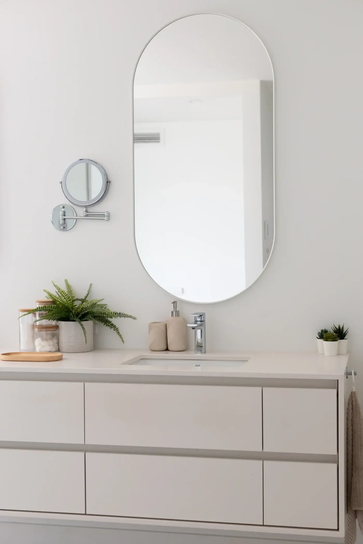 Détail de la vanité sur mesure blanche avec miroir ovale et accessoires déco.